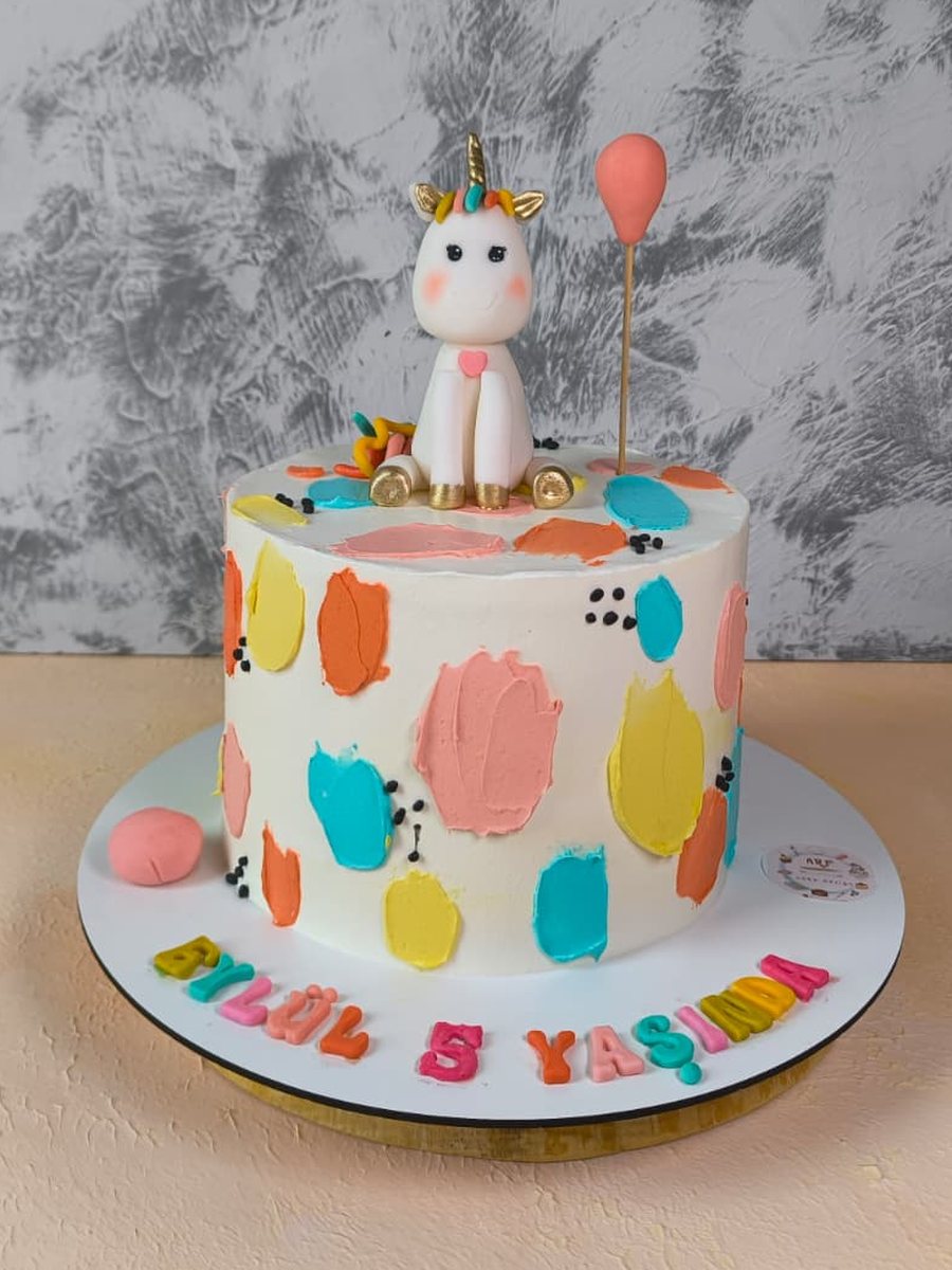 Renkli krema lekeleriyle süslü, üzerinde unicorn figürü ve balon olan çocuk doğum günü pastası