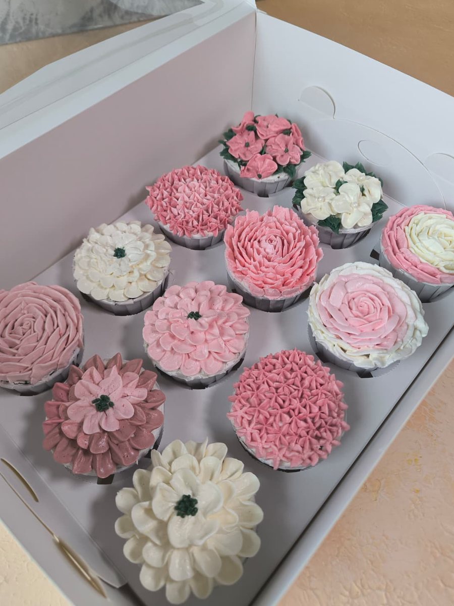 Kutusunda, pembe ve beyaz krema ile gül, şakayık ve kasımpatı gibi çiçekler sıkılmış on iki cupcake